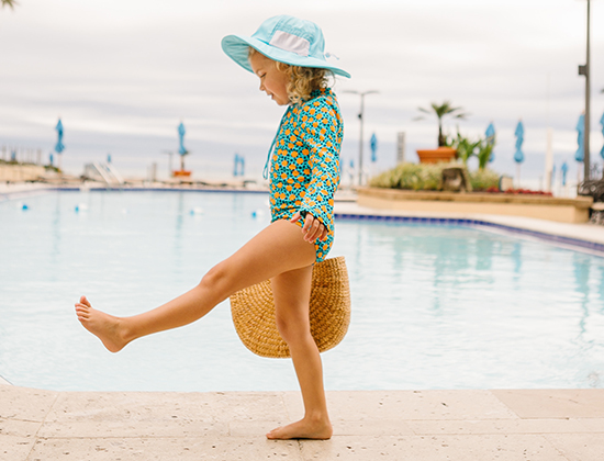 kid by pool walking with a beach bag