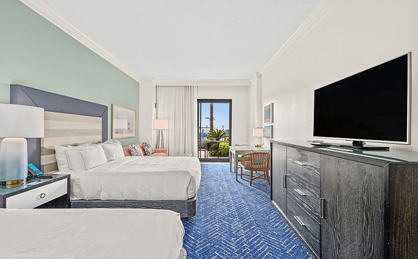 Two beds in a hotel room with a desk and tv